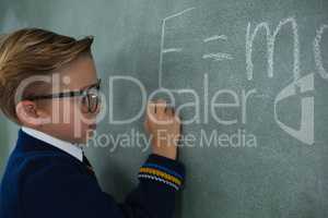 Schoolboy writing maths formula on chalkboard