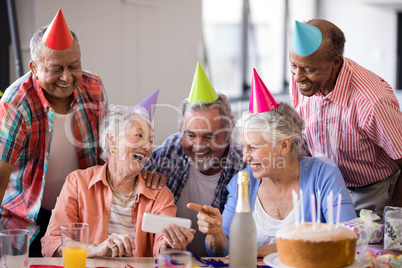 Cheerful senior woman showing mobile phone to friends in party