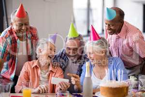 Cheerful senior woman showing mobile phone to friends in party
