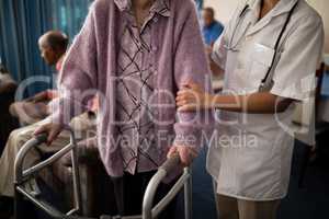 Midsection of female doctor helping senior woman standing with walker