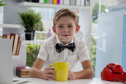 Smiling businessman holding yellow coffee mug at desk