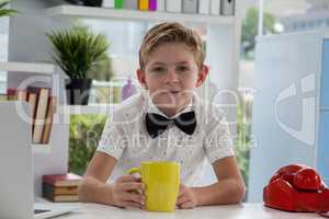 Smiling businessman holding yellow coffee mug at desk