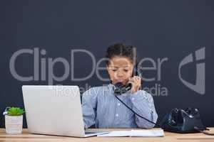 Businesswoman using landline phone while working on laptop
