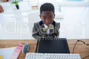 High angle portrait of boy imitating as businessman sitting at desk