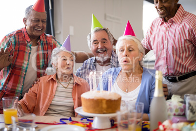 Friends looking at senior woman blowing birthday candles