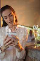 Smiling woman using mobile phone while having a glass of champagne