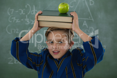 Schoolboy holding books stack with apple against chalkboard