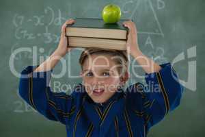 Schoolboy holding books stack with apple against chalkboard