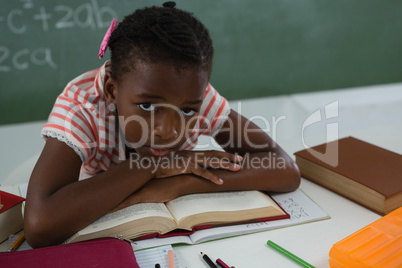 Schoolgirl relaxing on an open book in classroom