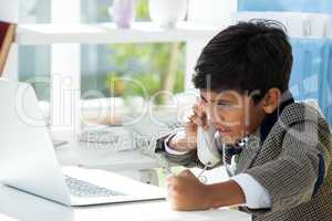 Serious businessman talking on telephone while looking at laptop