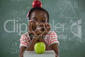 Schoolgirl sitting with red apple on her head against chalkboard