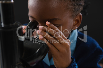 Schoolgirl using microscope against black background