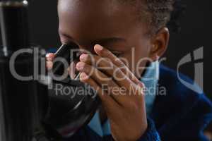 Schoolgirl using microscope against black background