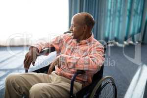 Smiling disabled senior man sitting on wheelchair against window