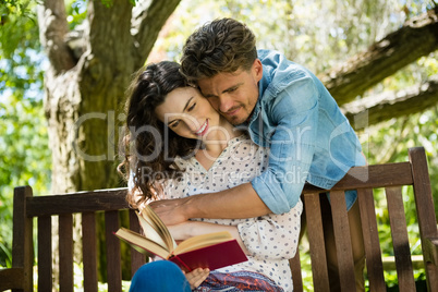 Romantic couple reading book on bench in garden