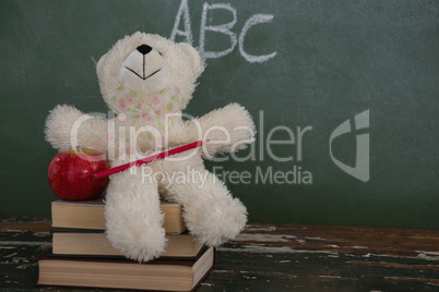 Teddy bear, pencil and apple on stack of books