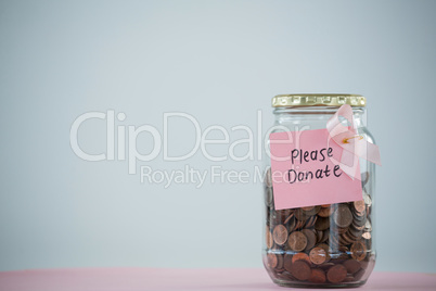 Close-up of card and pink Breast Cancer Awareness ribbon on jar with coins on table