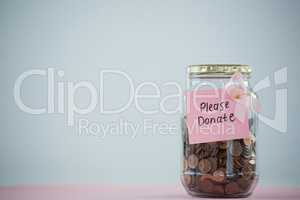 Close-up of card and pink Breast Cancer Awareness ribbon on jar with coins on table