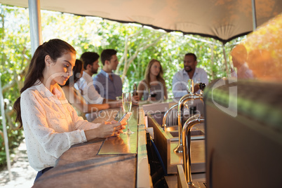 Smiling woman using mobile phone while having a glass of champagne