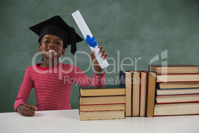 Schoolgirl in mortar board holding certificate against chalkboard