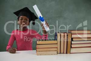 Schoolgirl in mortar board holding certificate against chalkboard