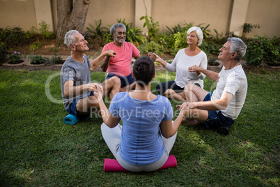 Trainer and senior people meditating while holding hands