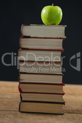 Green apple on book stack against black background