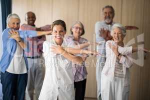Portrait of smiling female doctor and seniors stretching arm against wall