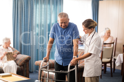 Female doctor assisting senior man walking with walker