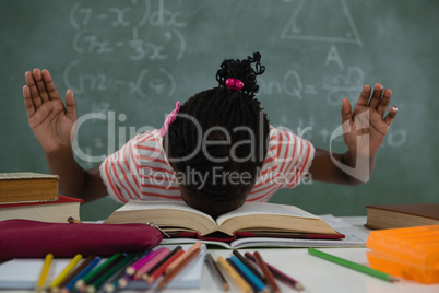 Schoolgirl lying on an open books in classroom