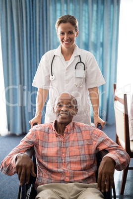 Portrait of smiling female doctor standing with disabled senior man sitting on wheelchair