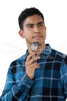 Close up of thoughtful young man holding eyeglasses while looking away