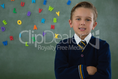 Schoolboy standing with arms crossed against chalkboard