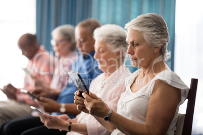 Row of senior people sitting on chairs using digital tablets