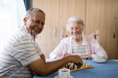 Smiling senior man playing chess with friend