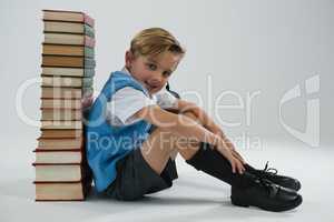 Schoolboy sitting against books stack on white background
