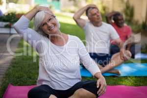 Smiling woman stretching head while exercising with friends
