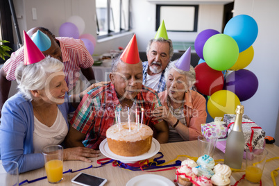 Senior man blowing candles on birthday cake