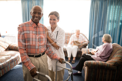 Portrait of smiling female doctor standing by senior man with walker against window Portrait of smiling female doctor standing by senior man with walker against window