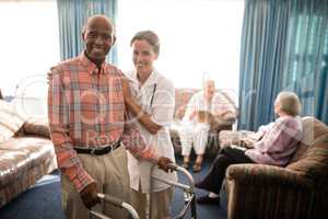 Portrait of smiling female doctor standing by senior man with walker against window