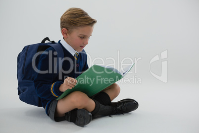 Schoolboy reading book while sitting on white background