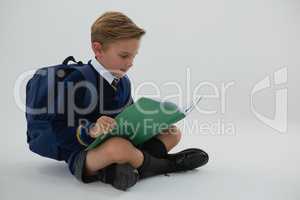 Schoolboy reading book while sitting on white background