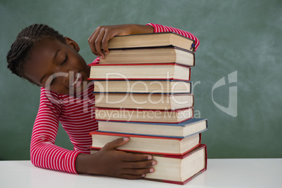 Schoolgirl sitting with books stack against chalkboard