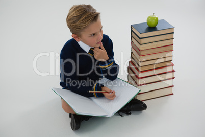 Schoolboy doing his homework while sitting beside books stack