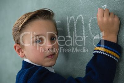 Schoolboy writing maths formula on chalkboard