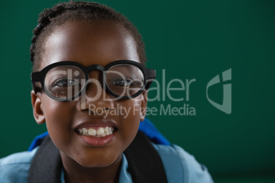 Smiling schoolgirl with spectacles standing against green background Smiling schoolgirl with spectacles standing against green background