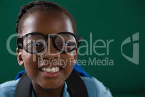 Smiling schoolgirl with spectacles standing against green background