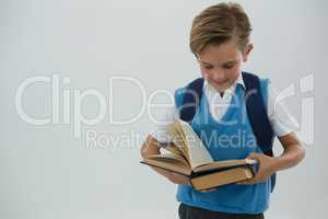 Schoolboy reading book against white background