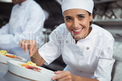 Female chef garnishing food in kitchen at restaurant