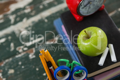 Alarm clock, apple and chalk on stack of books with pen holder